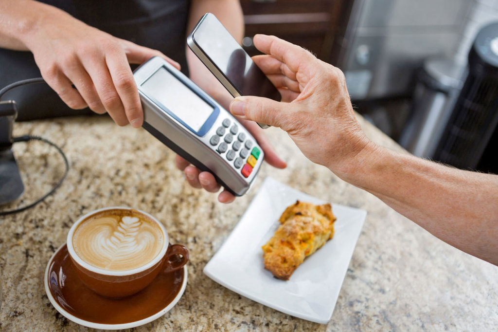 Cropped image of customer paying through mobilephone over electronic reader at cafe counter